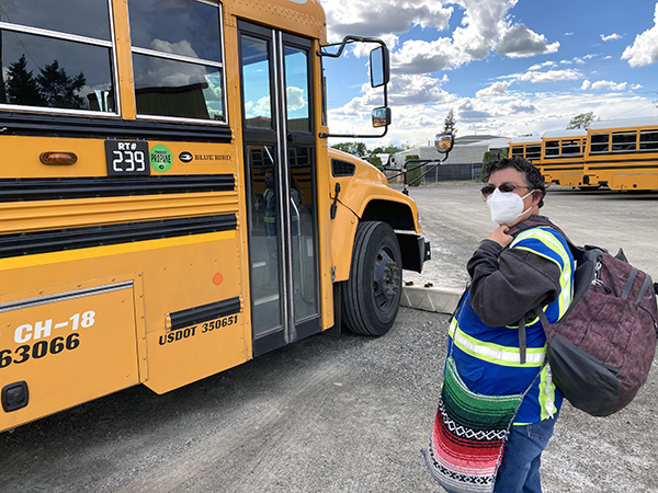 Molly in front of a yellow school bus with a mask on and her bags