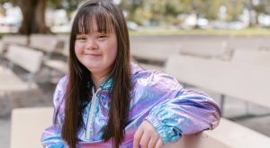 Woman with down syndrome sitting in an open area with a purple reflective jacket