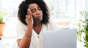 Burnout & Employment: Woman sitting in front of a laptop with her eyes closed and her head in her hand looking stressed