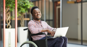 Photo of black man in a wheelchair with a laptop in his lap smiling.